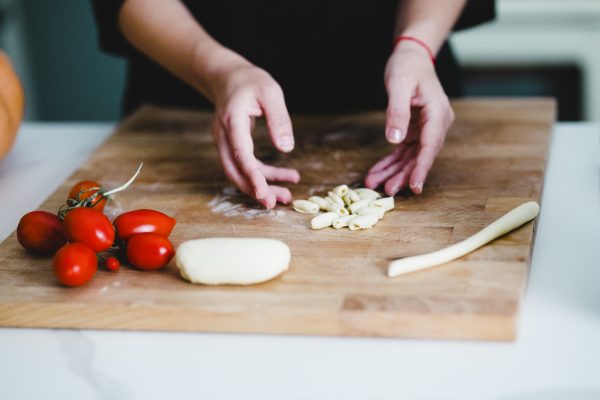 Hands shaping fresh Sicilian pasta with tomatoes on a wooden board